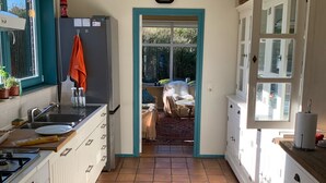 Eine Küche mit weißen Schränken, Fliesenboden, Spüle und einem Fenster mit Gartenblick.