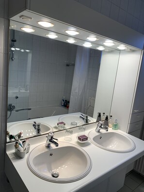 Ein modernes Badezimmer mit zwei Waschbecken, einem großen Spiegel und Deckenleuchten.