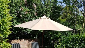 Eine Terrasse mit zwei gestreiften Liegestühlen und einem beigen Sonnenschirm.