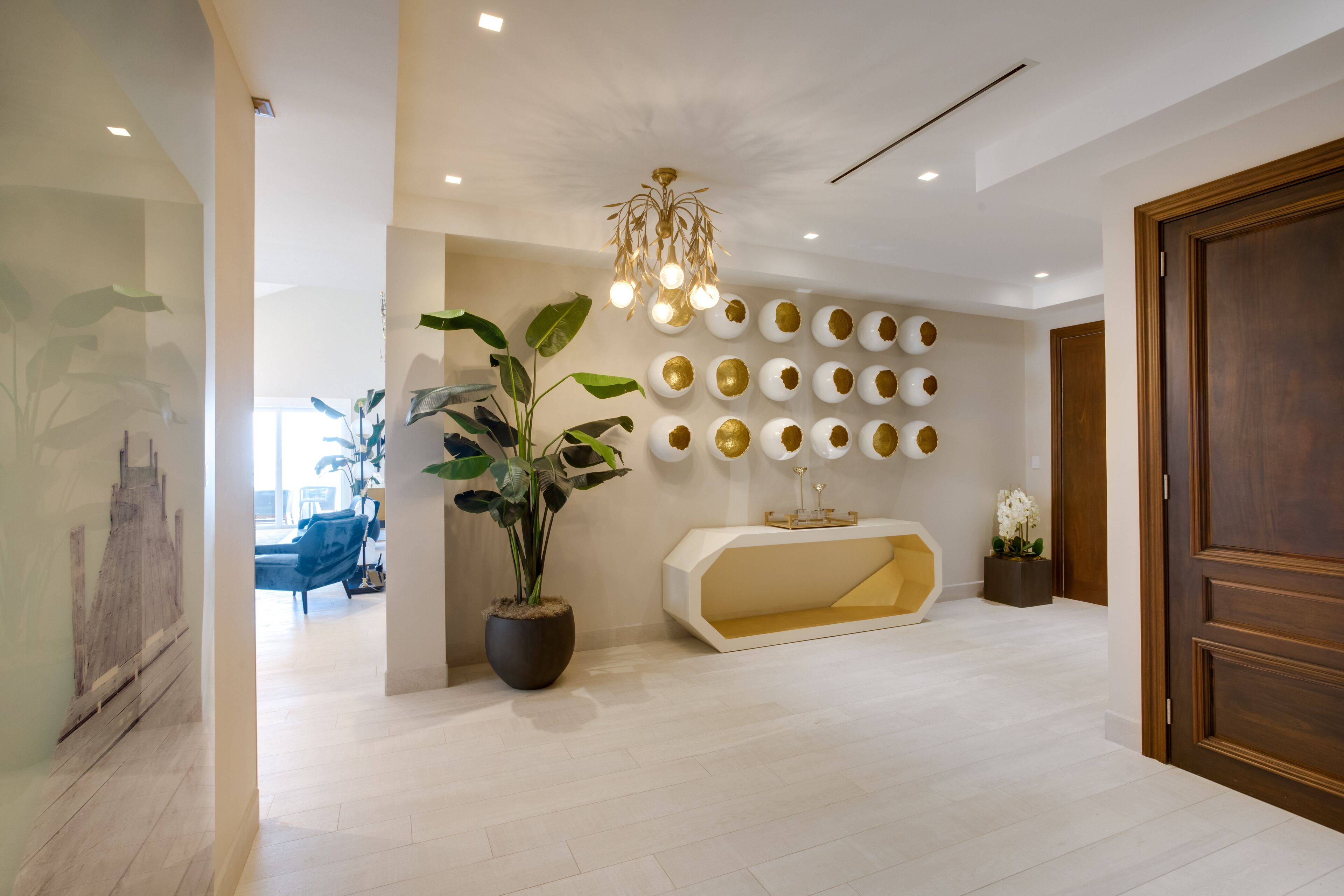 Una recepción moderna con una consola central, una planta en maceta grande y una pared decorada con platos.
