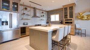 A modern kitchen with stainless steel appliances, a central island with bar stools, and a decorative gold piece on the wall.