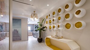 A modern reception area with a white and yellow console, a large potted plant, and a wall decorated with white plates with gold centers.