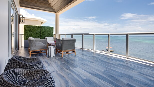 A balcony with wicker furniture, a green wall, and a view of the sea.