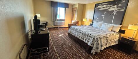 Habitación de hotel con cama, escritorio, silla y una ventana grande con cortinas.