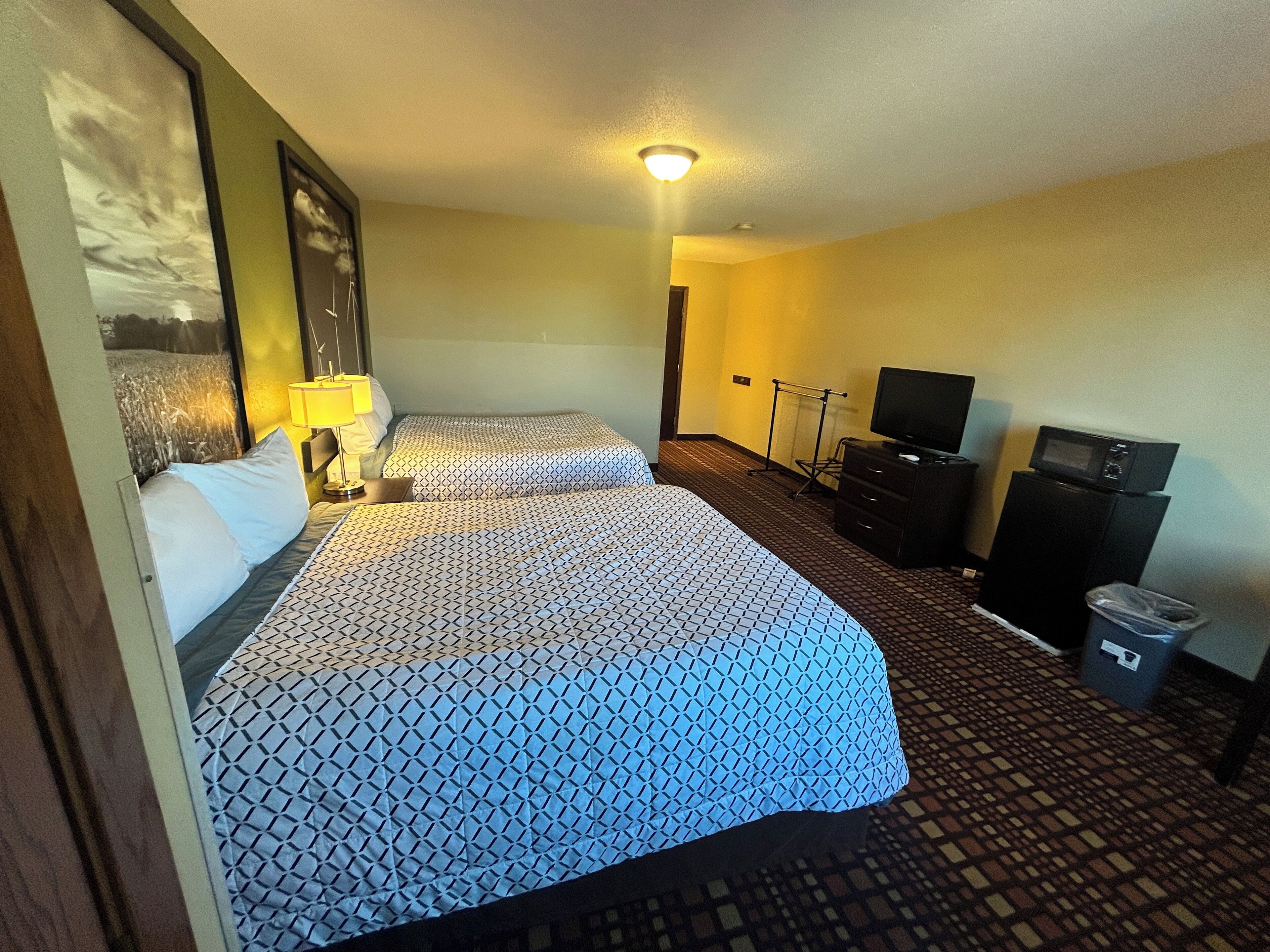 A hotel room with two beds, a television, a trash bin, and a small desk.