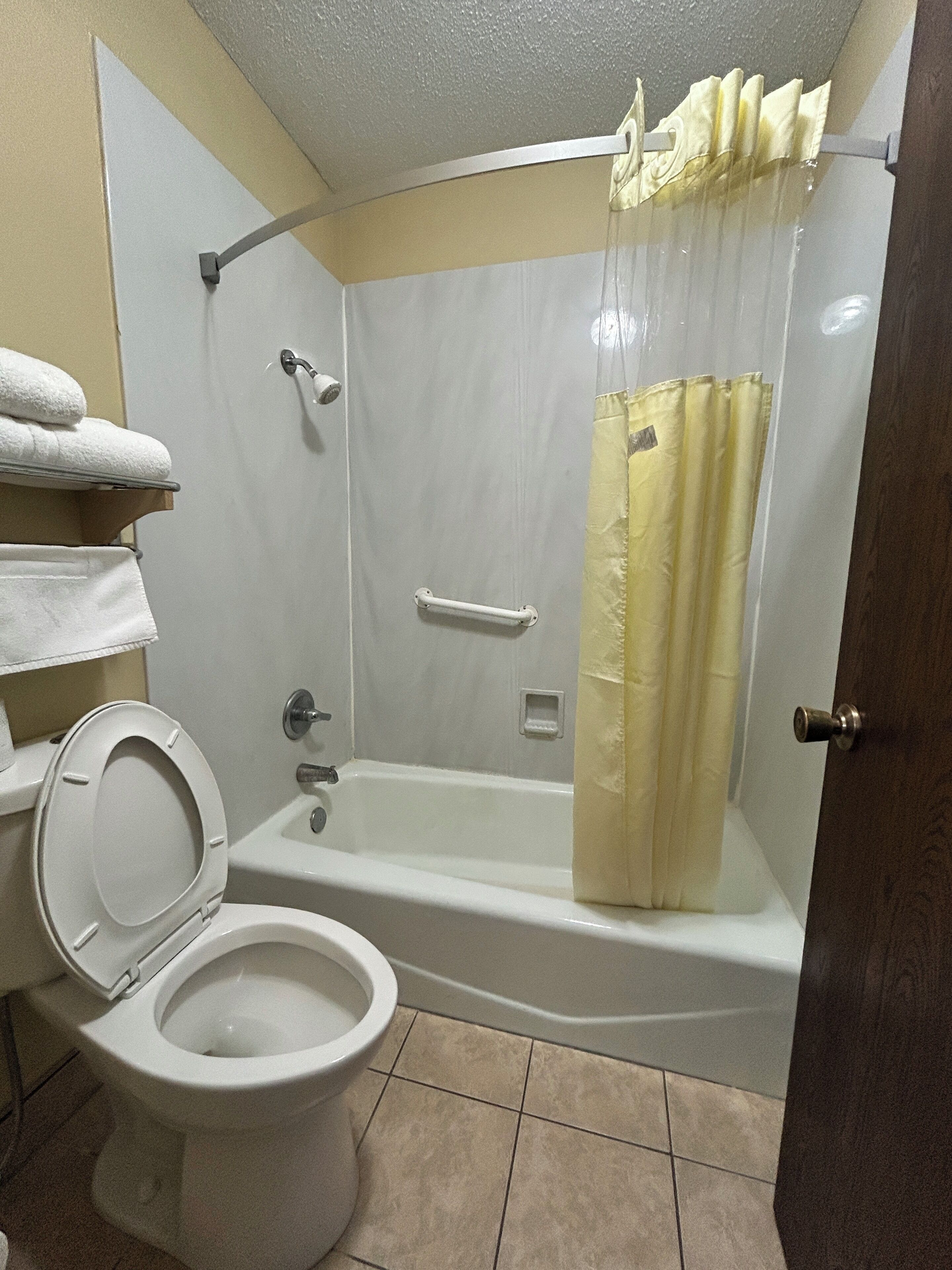 A bathroom with a toilet, a shower with a curtain, and a towel rack with towels.