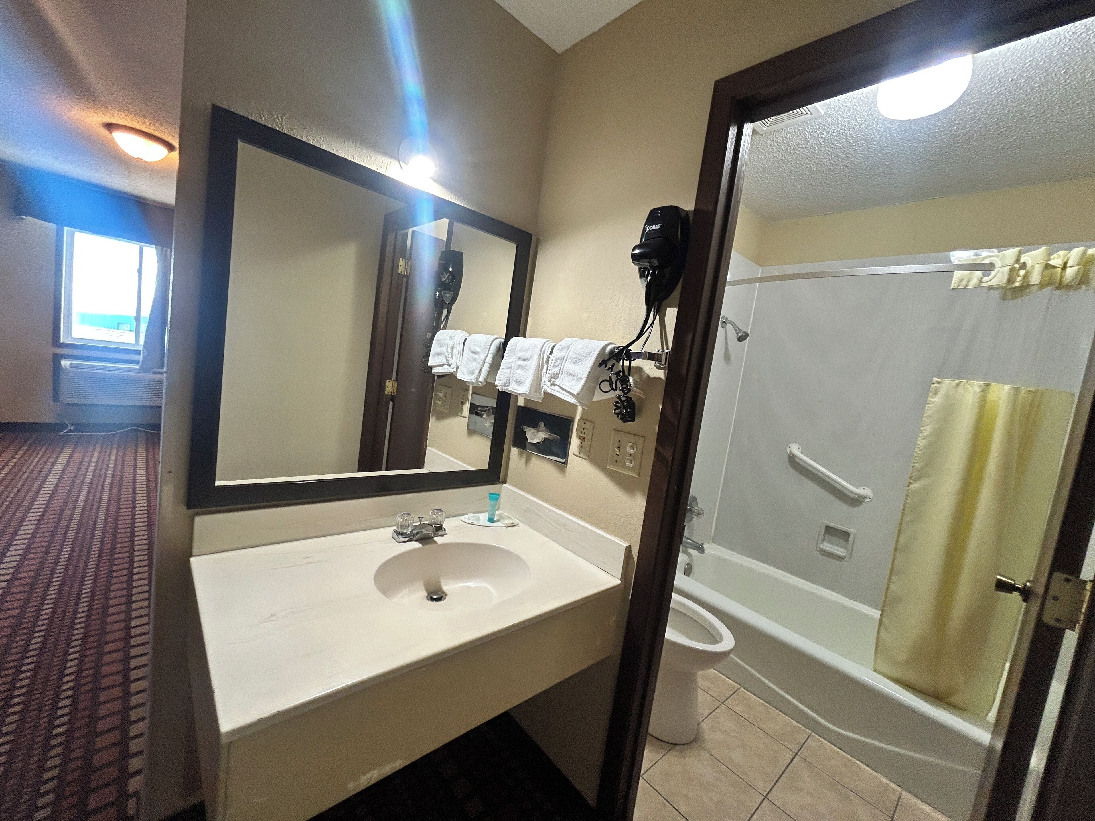 Un baño de hotel con lavamanos, espejo, toallero y zona de ducha.
