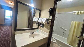 Un baño de hotel con lavamanos, espejo, toallero y zona de ducha.