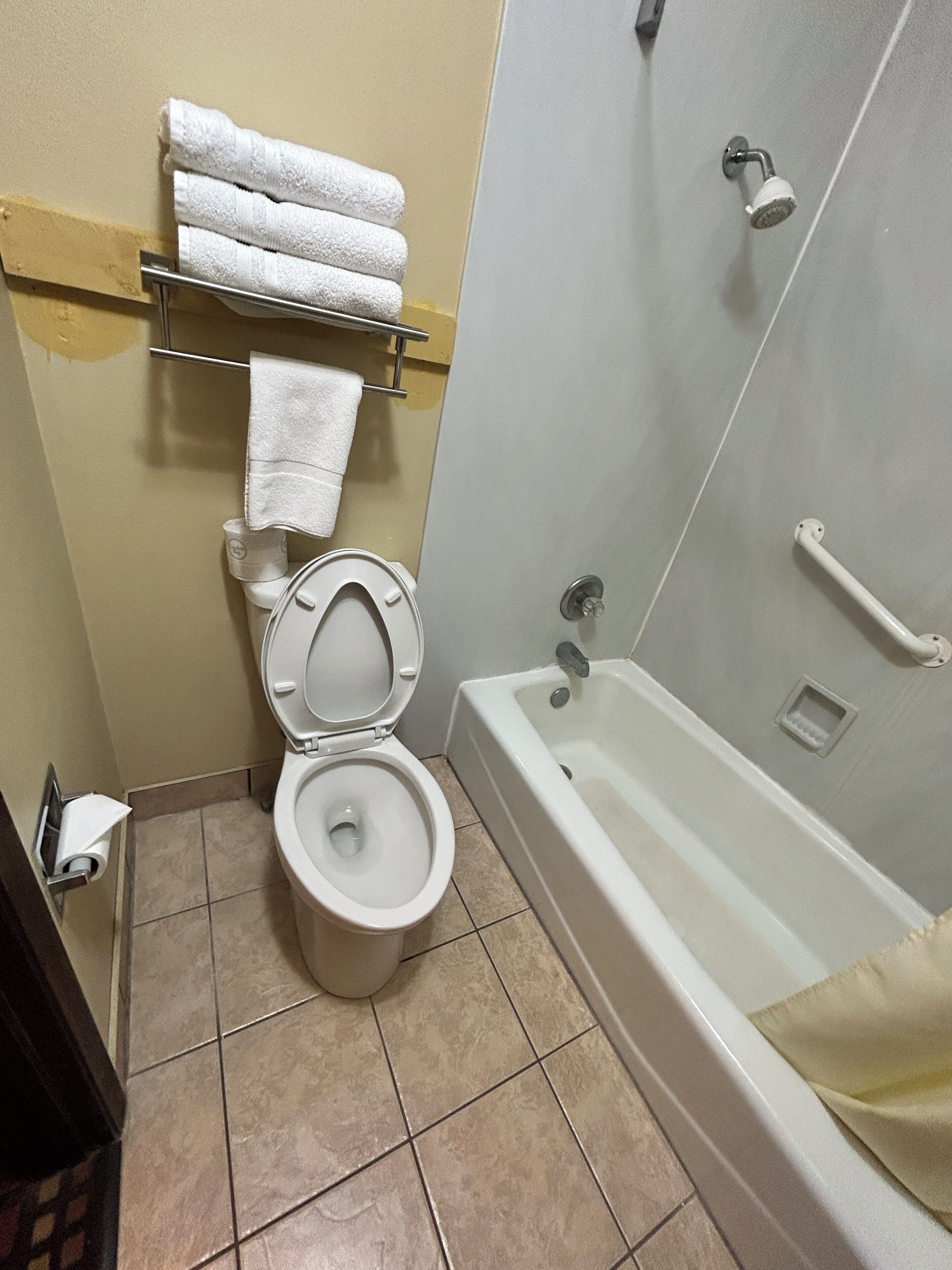 Un bagno con il water, un portasciugamani con asciugamani piegati, una vasca e un soffione.