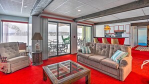 A spacious living room with a red carpet, a large sofa, a coffee table, and a view through a glass door to a snowy outdoor area.