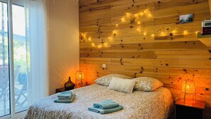 A bedroom with a wooden headboard, a bed with patterned bedding, two bedside lamps, and a window with a view of outdoor furniture.