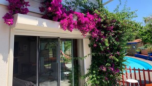 A house with a sliding glass door, a pool, and vibrant pink bougainvillea flowers climbing the exterior wall.