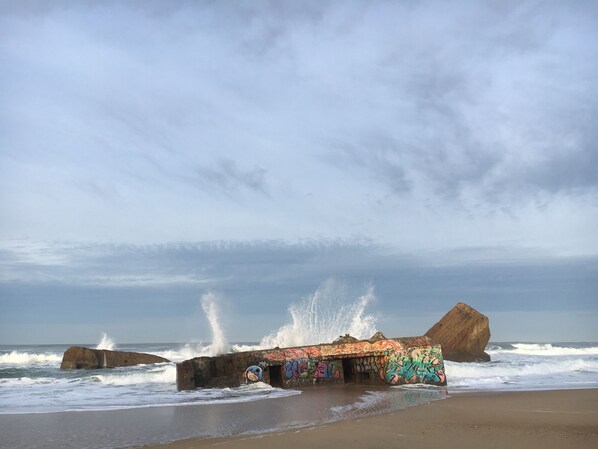 A beach with a graffiti-covered structure partially submerged in waves.