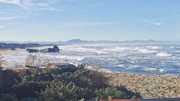 A beach with waves, a sandy shore, and a structure in the distance.