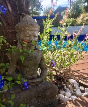 Une statue de pierre représentant une figure assise, entourée de verdure et de fleurs.