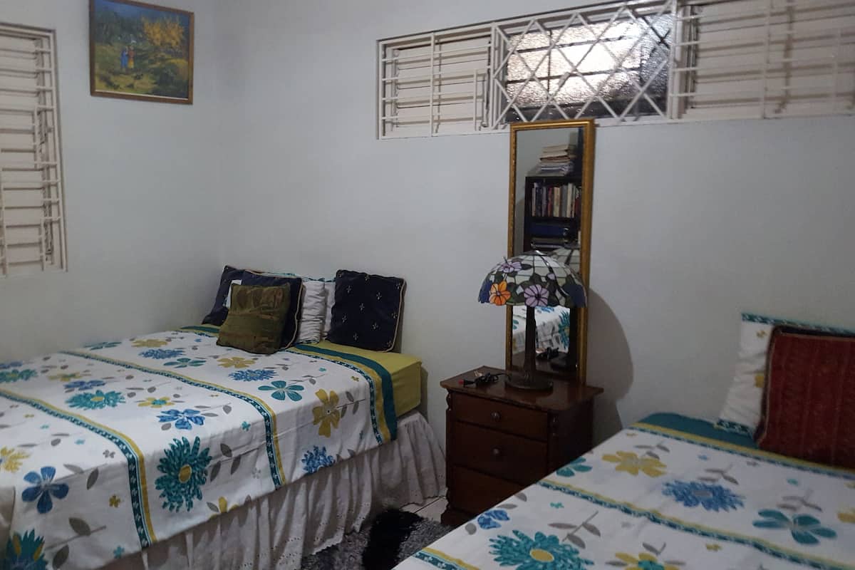 A bedroom with two beds, a nightstand, a mirror, and a window with blinds.