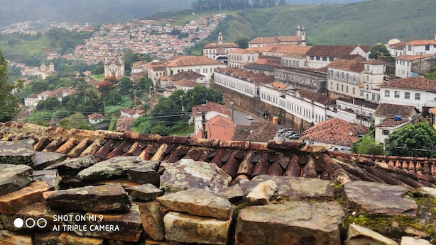 A historic town with terracotta-roofed buildings, cobblestone streets, and a prominent church tower. - Diamond Hostel (Ouro Preto)