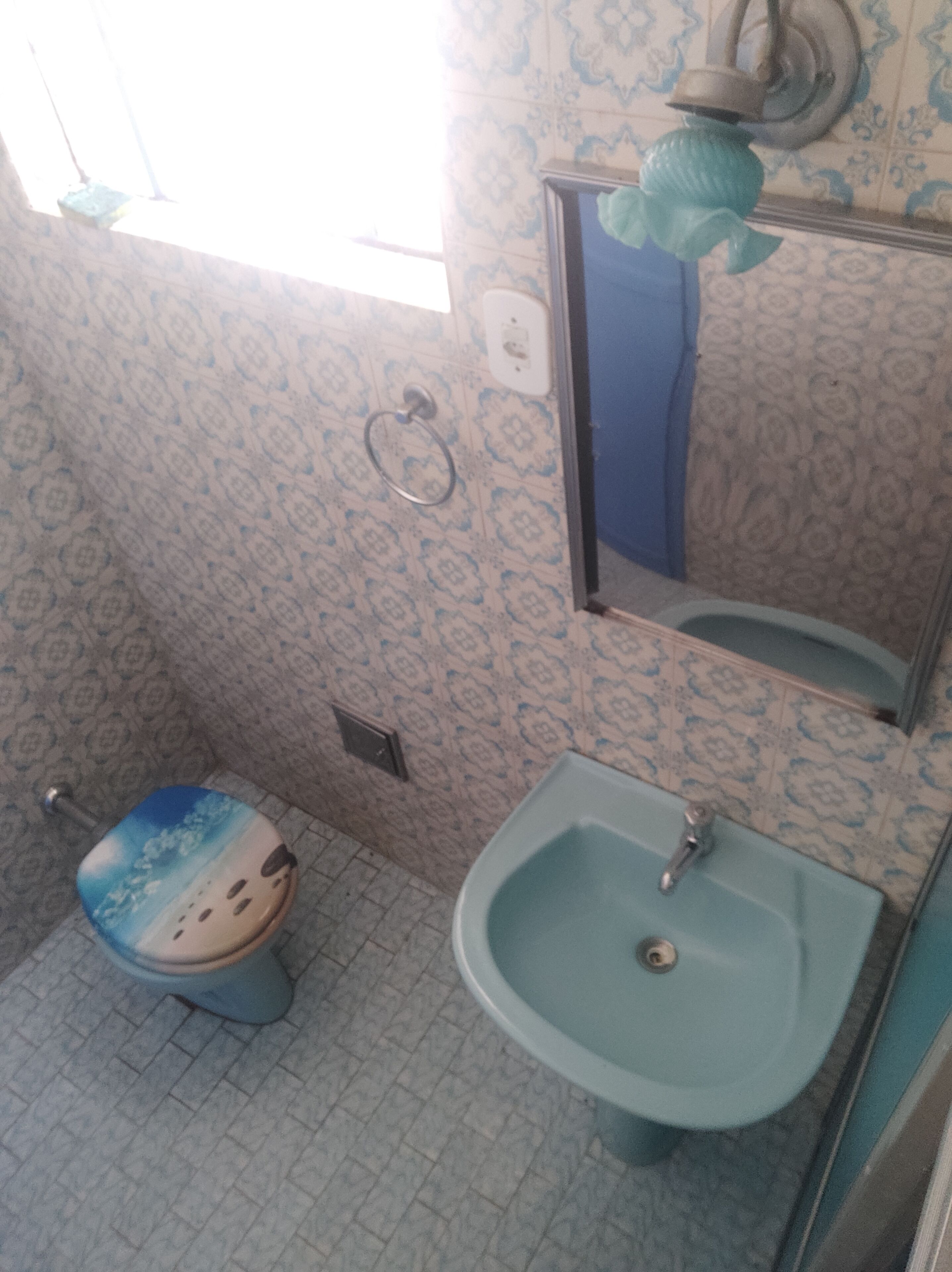 Ein Badezimmer mit gemusterten Fliesen, einer Toilette mit Cartoon-Gesicht, einem Waschbecken und einem Spiegel.