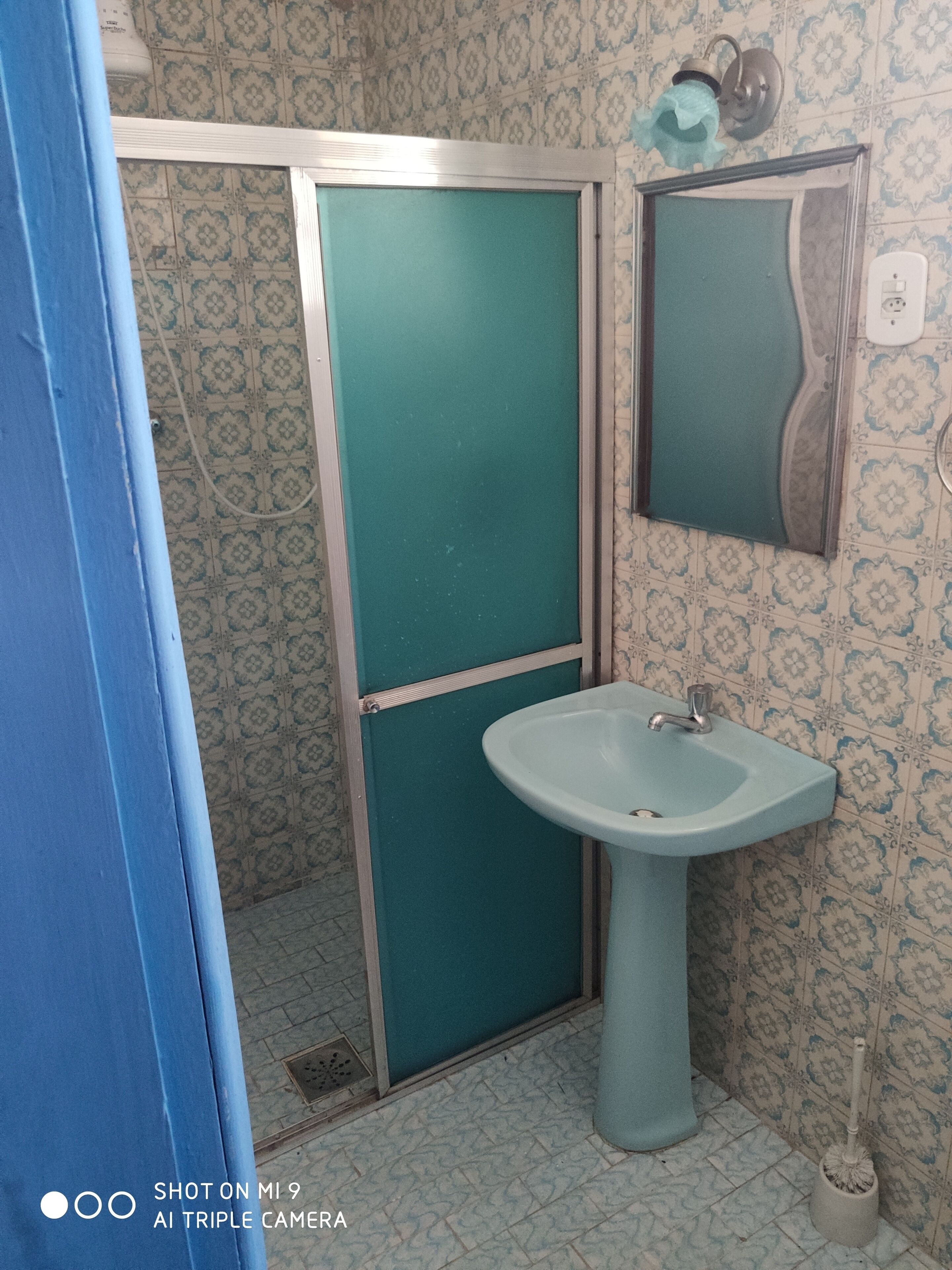 Un baño con una puerta color turquesa, un lavamanos y un espejo.