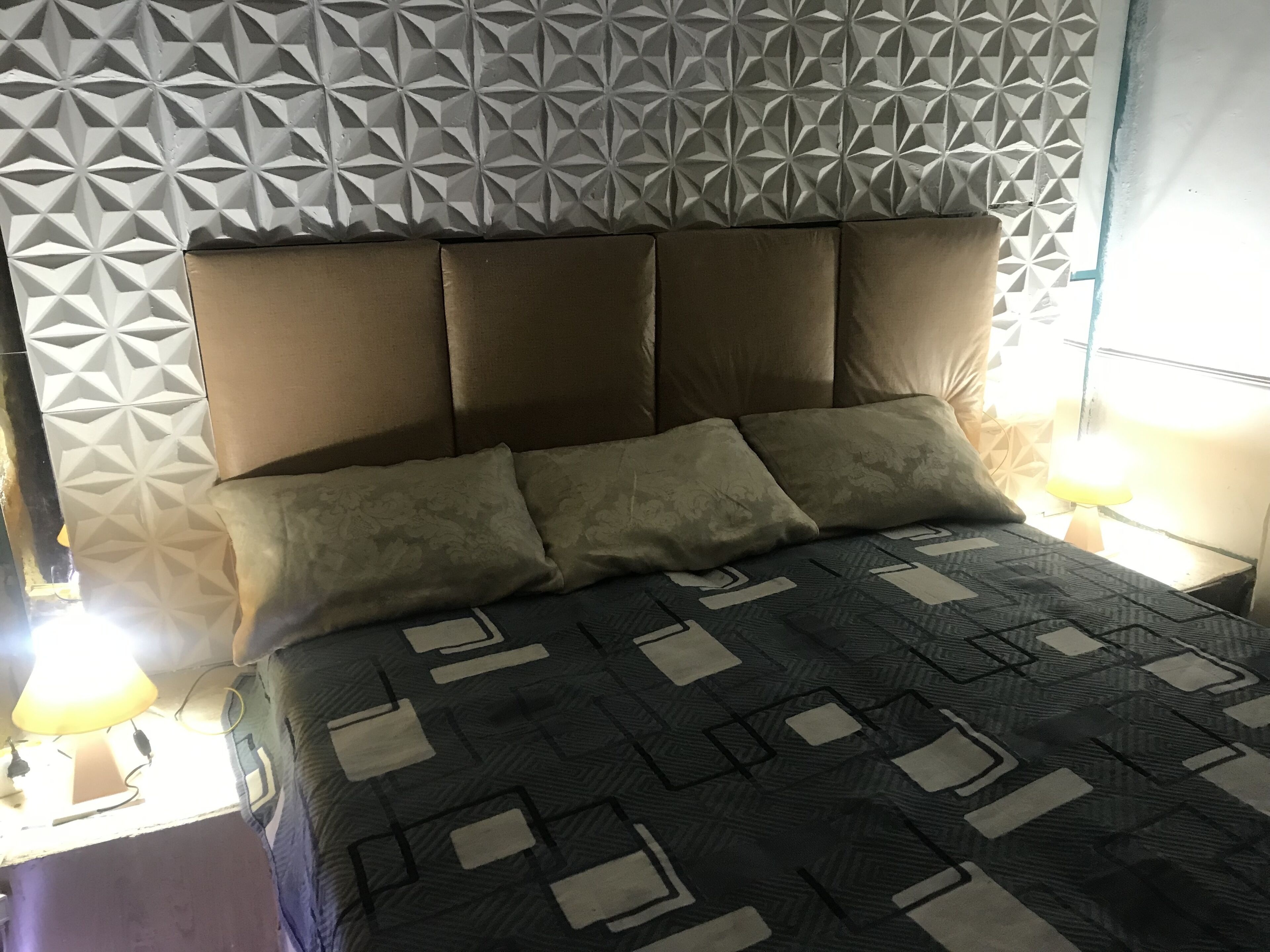 A bed with a geometric patterned bedspread, a headboard with a geometric design, and two bedside lamps.