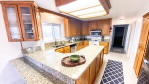 A modern kitchen with granite countertops, wooden cabinets, and a central island. - The Gathering Place on the Teton River (Rexburg)