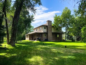 Set amidst a lush lawn and shaded by trees, this charming home features a covered porch and a prominent chimney.