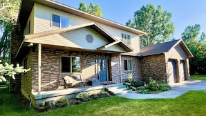 A two-story house with a brick facade, a front porch with a bench, and a garage. - The Gathering Place on the Teton River (Rexburg)