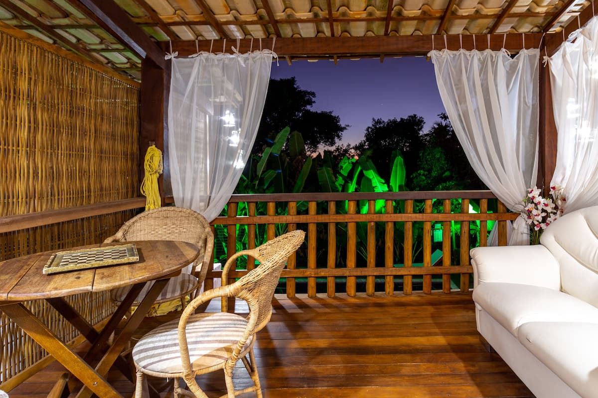 Un espacio de estar al aire libre cubierto con piso de madera, muebles de mimbre y un sofá blanco.