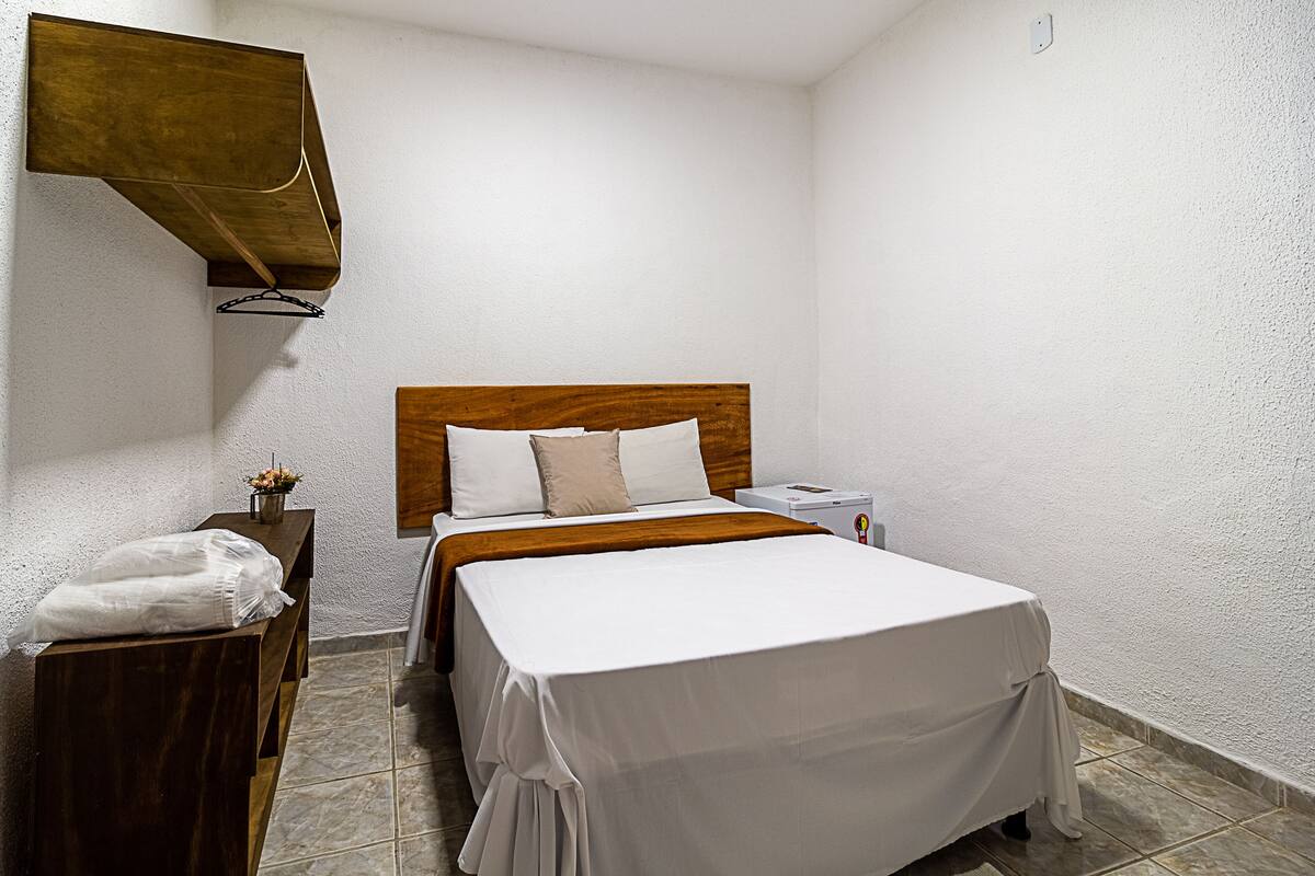 Una cama bien hecha con cabecera de madera, una mesita de noche con lámpara y un pequeño atril con lámpara.