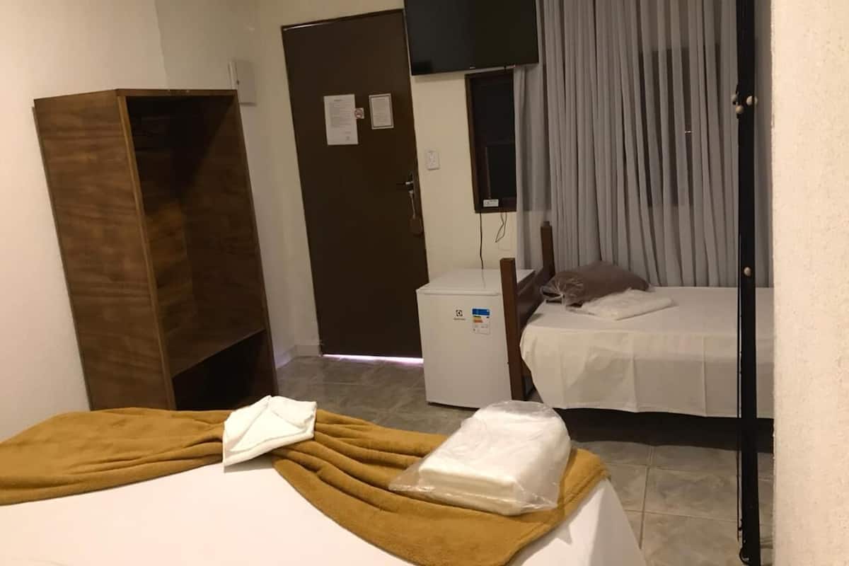 Habitación de hotel con cama, escritorio pequeño, armario, nevera y puerta de baño.