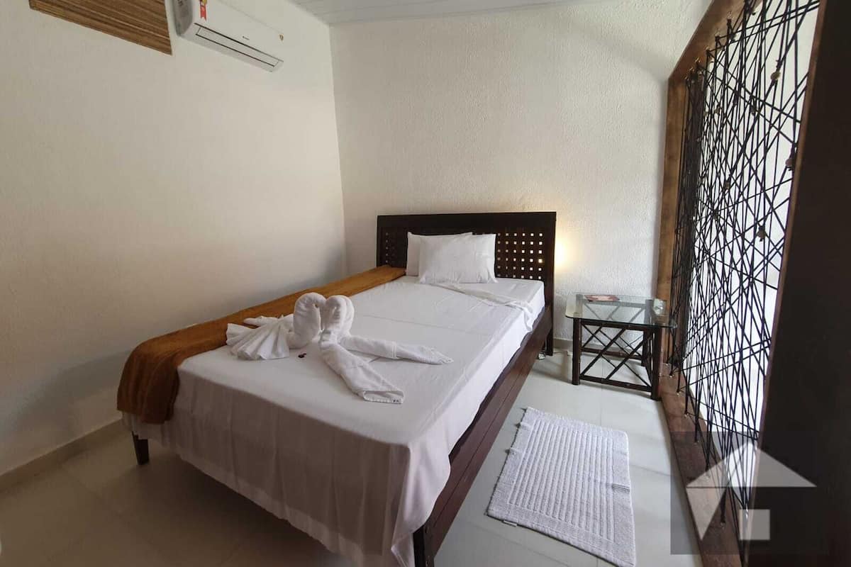Habitación de hotel con cama, mesita de noche, aire acondicionado instalado en la pared y un biombo decorativo de metal.