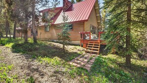 A log cabin with a red roof, surrounded by trees and a small wooden deck.