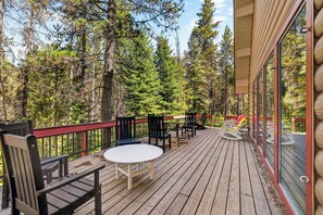 A wooden deck with outdoor seating, surrounded by trees.