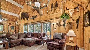 A cozy cabin interior with a sectional sofa, leather armchair, and a small wooden cabinet.