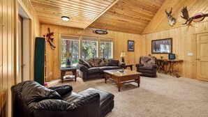 A log cabin interior with a wooden ceiling, leather furniture, a fireplace, and a large window.