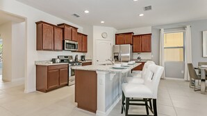 A modern kitchen with wooden cabinets, stainless steel appliances, and a central island with bar stools. - Star Wars & Princess Themed • South-Facing Pool & Spa • Game Room • Gated Resort (Davenport)