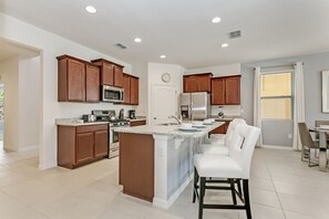 A modern kitchen with wooden cabinets, stainless steel appliances, and a central island with bar stools. - Star Wars & Princess Themed • South-Facing Pool & Spa • Game Room • Gated Resort (Davenport)