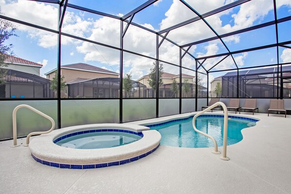 An indoor swimming pool with a hot tub, surrounded by a glass enclosure, and a view of houses in the background. - Star Wars & Princess Themed • South-Facing Pool & Spa • Game Room • Gated Resort (Davenport)