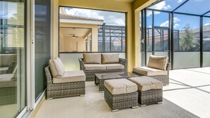 Ein sonniger Balkon mit Korbmöbeln, darunter eine Couch und Hocker, und eine Glastür, die zu einer Terrassenfläche führt.