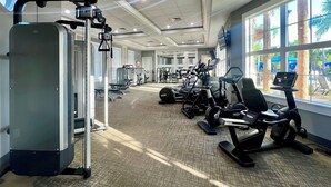 A gym with cardio machines, weight stations, and a large window with a view of palm trees. - Star Wars & Princess Themed • South-Facing Pool & Spa • Game Room • Gated Resort (Davenport)