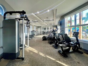 A gym with cardio machines, weight stations, and a large window with a view of palm trees. - Star Wars & Princess Themed • South-Facing Pool & Spa • Game Room • Gated Resort (Davenport)