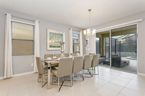 A dining area with a table set for six, a chandelier, and a sliding glass door leading to an outdoor seating area.
