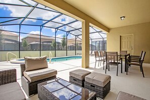 Área externa coberta com mobiliário de vime, piscina e vista para casas vizinhas.