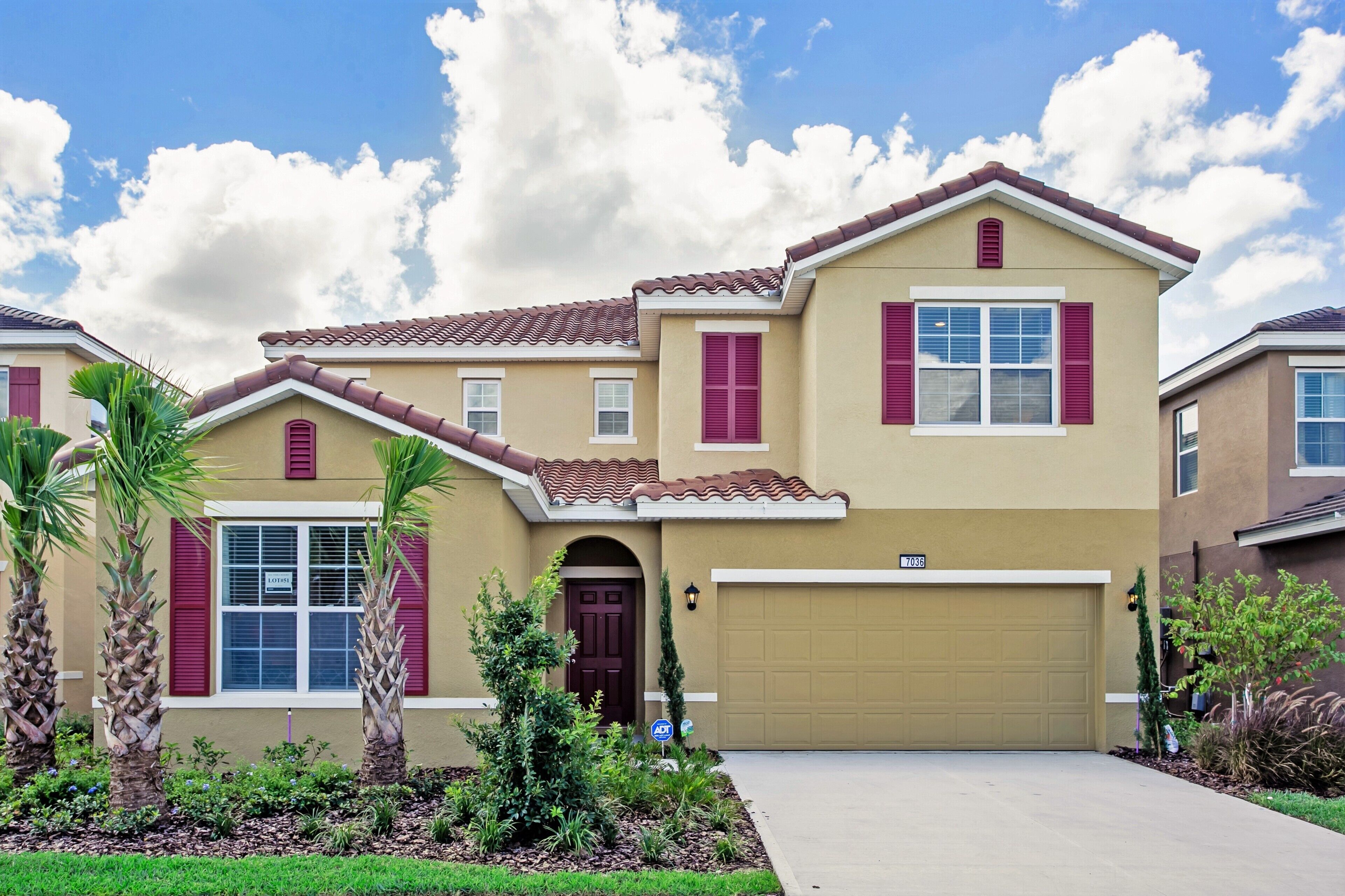 A two-story house with a beige facade, red shutters, and a brown roof.