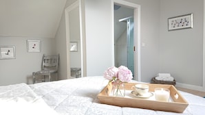 A bedroom with a bed, a wooden tray with a vase of flowers, a cup, and a candle. There are two chairs, a framed picture on the wall, and a bathroom visible through an open door. - Luxurious and Spacious 5 Bedroom Self-Catering House in Doolin. 3250 Square ft	. (Doolin)