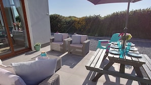 An outdoor patio area with wicker furniture, a wooden table, and a large umbrella. - Luxurious and Spacious 5 Bedroom Self-Catering House in Doolin. 3250 Square ft	. (Doolin)