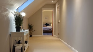 A hallway with a sloped ceiling, a small table with a plant, and a bed in the background. - Luxurious and Spacious 5 Bedroom Self-Catering House in Doolin. 3250 Square ft	. (Doolin)