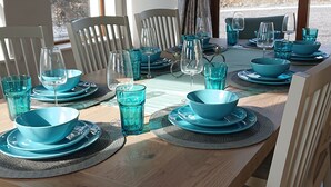 A dining table set with blue glassware and plates, white chairs, and a view of the outdoors through large windows. - Luxurious and Spacious 5 Bedroom Self-Catering House in Doolin. 3250 Square ft	. (Doolin)