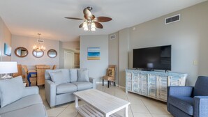 Ein Wohnzimmer mit einer Couch, Sesseln, einem Couchtisch, einem Fernseher und einem Deckenventilator.