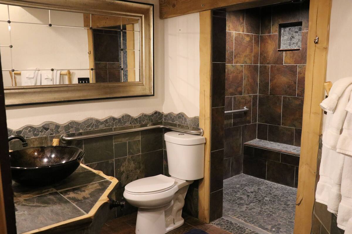Un baño con un espejo grande, un lavabo, un inodoro y una zona de ducha con paredes y suelo de baldosas.